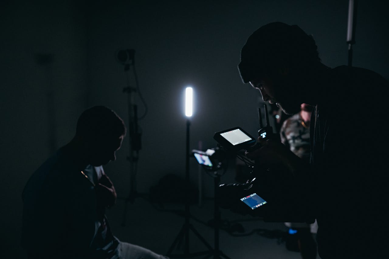 A low-light studio scene focusing on a cinematographer operating a camera with lighting equipment.